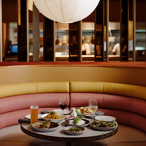 Restaurant booth with a table full of shared dishes and drinks in a warm, modern dining setting.