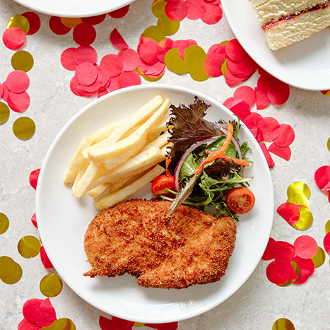 Breaded chicken schnitzel with fries and salad on a white plate with red and gold confetti.