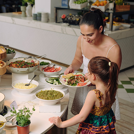 Woman and child serving themselves food from a buffet with fresh salads and dishes.